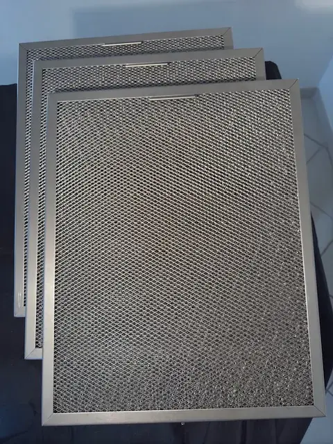 Filtres de hotte en métal, superposés et perforés, prêt à installation ou remplacement en cuisine professionnelle.